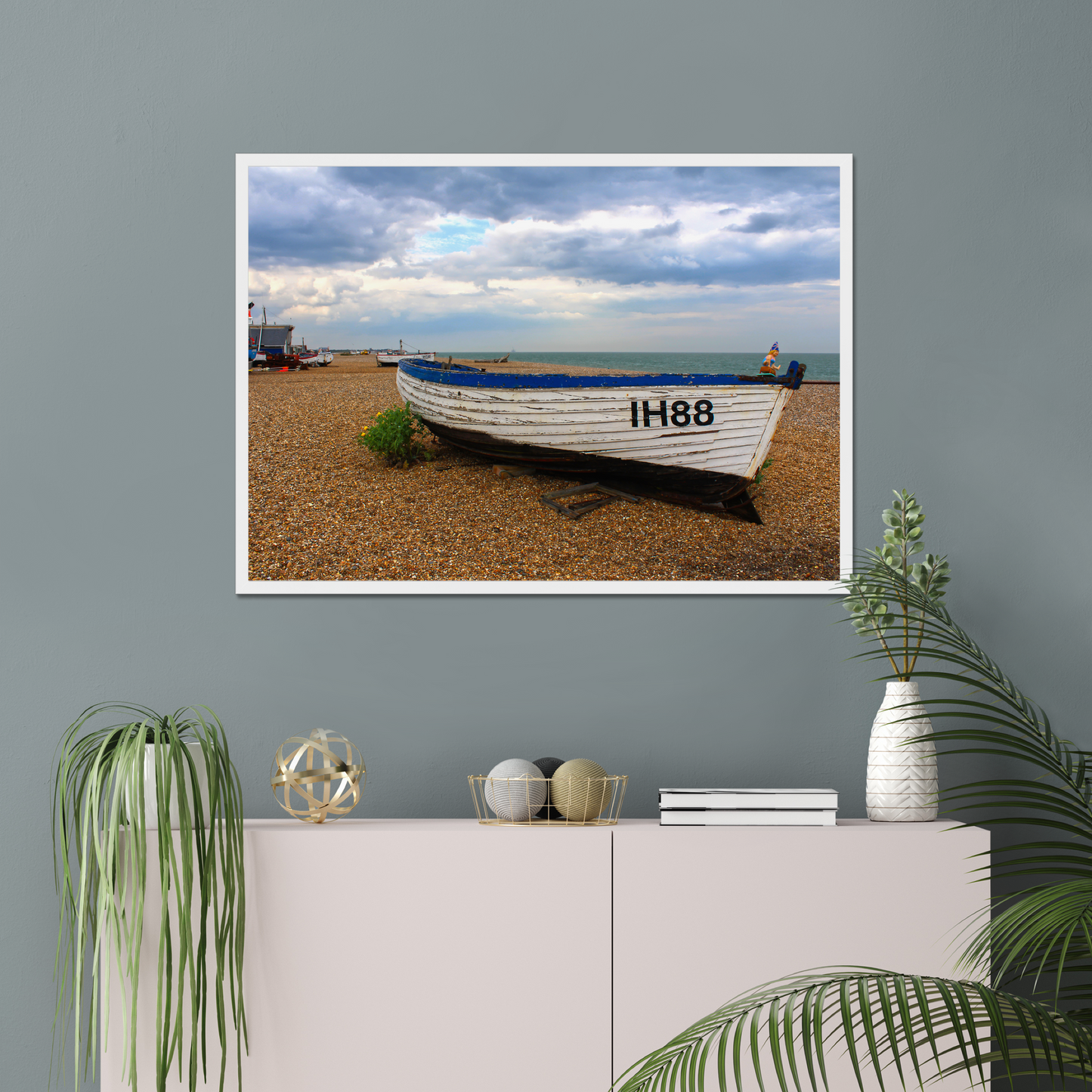Framed photograph of a boat on a beach wall-mounted above a white cabinet with decorative items.