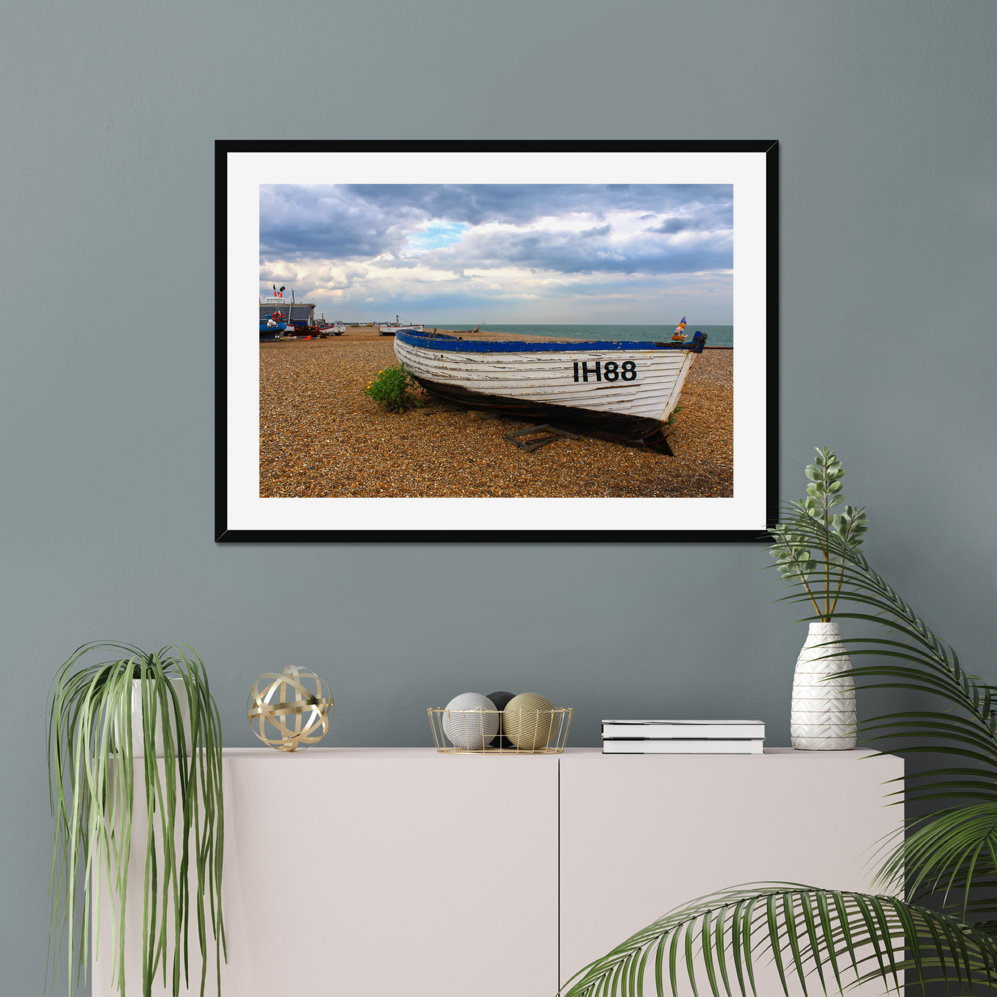 Framed photograph of a boat on a beach with decorative items on a shelf below.