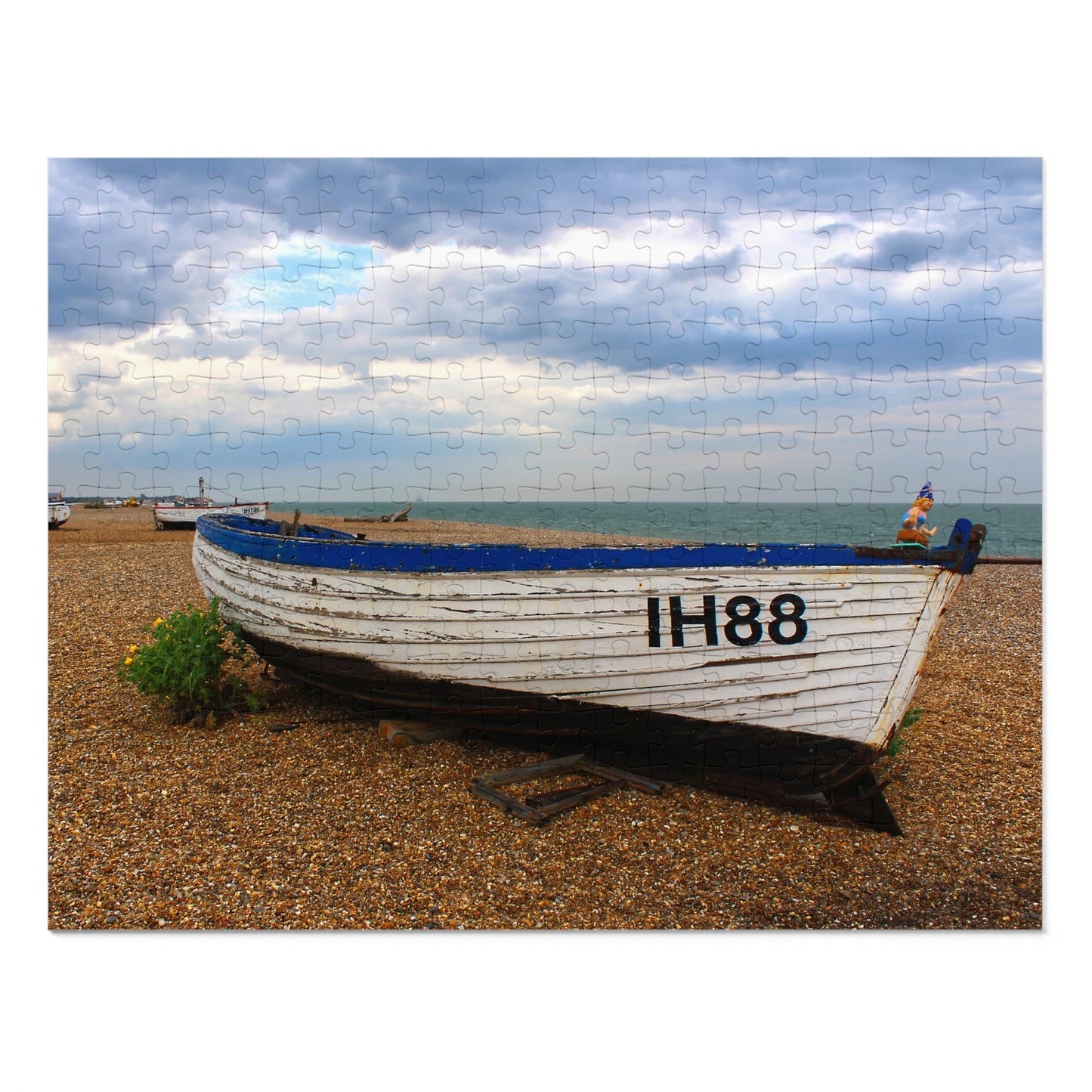 White boat with blue trim on a pebbly beach under a cloudy sky.