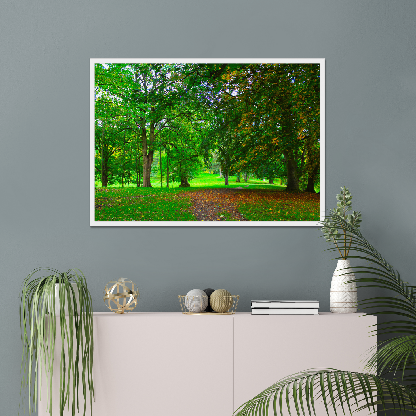 Framed nature print of a green forest scene on a gray wall above a white cabinet with decorative items.