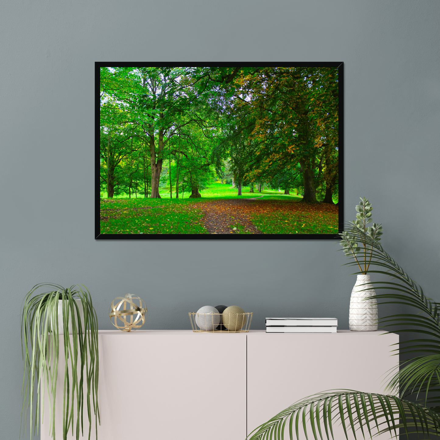Framed nature print of a green forest scene on a gray wall above a white cabinet with decorative items.