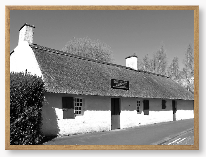 Black and White Framed Photo Of A Thatched cottage on a road with trees in the background