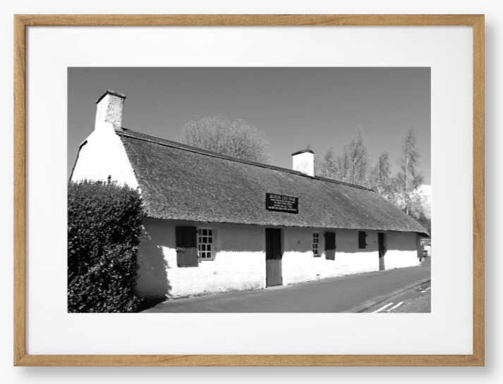 Black and White Framed Photo Of A Thatched cottage on a road with trees in the background