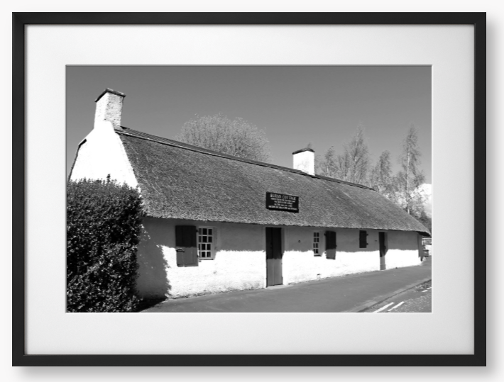Black and White Framed Photo Of A Thatched cottage on a road with trees in the background