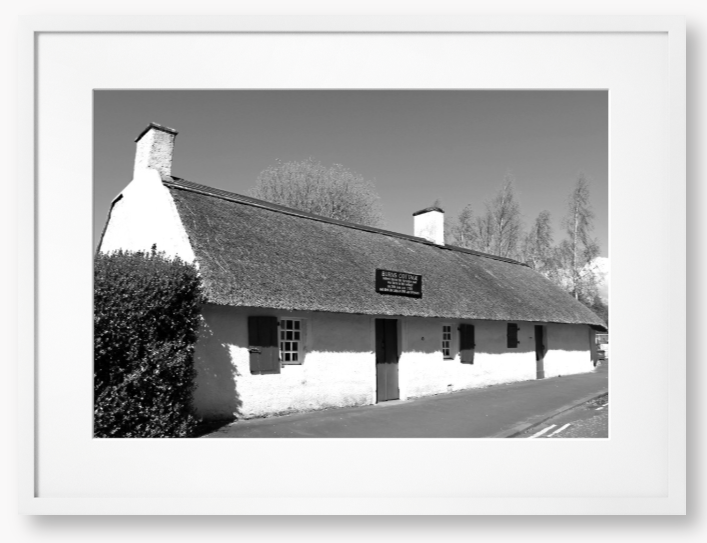 Black and White Framed Photo Of A Thatched cottage on a road with trees in the background