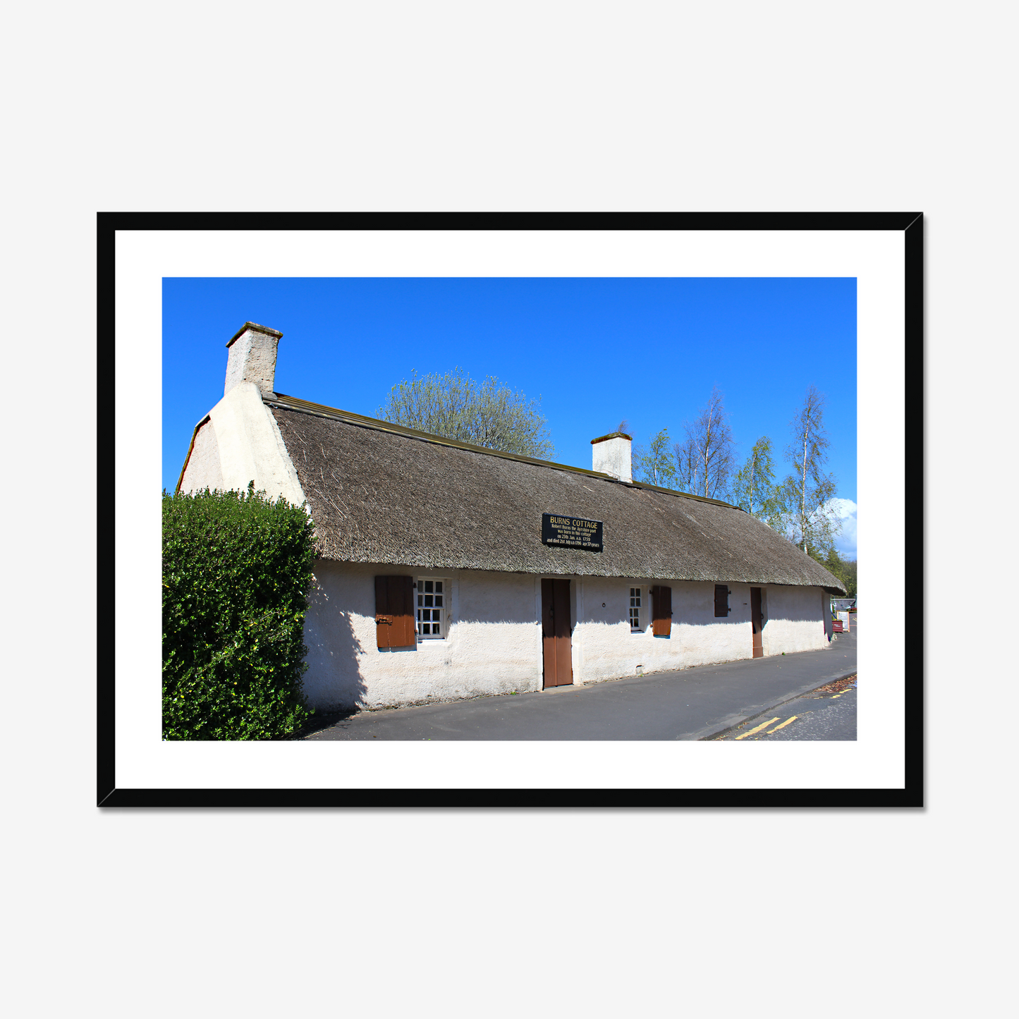 Framed picture of a thatched cottage with a clear blue sky.