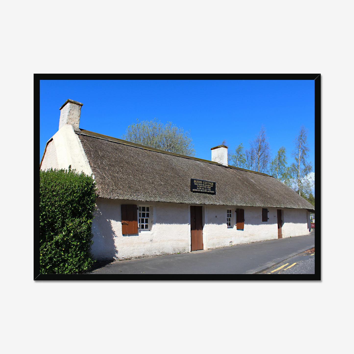 Framed picture of a thatched cottage with a clear blue sky.