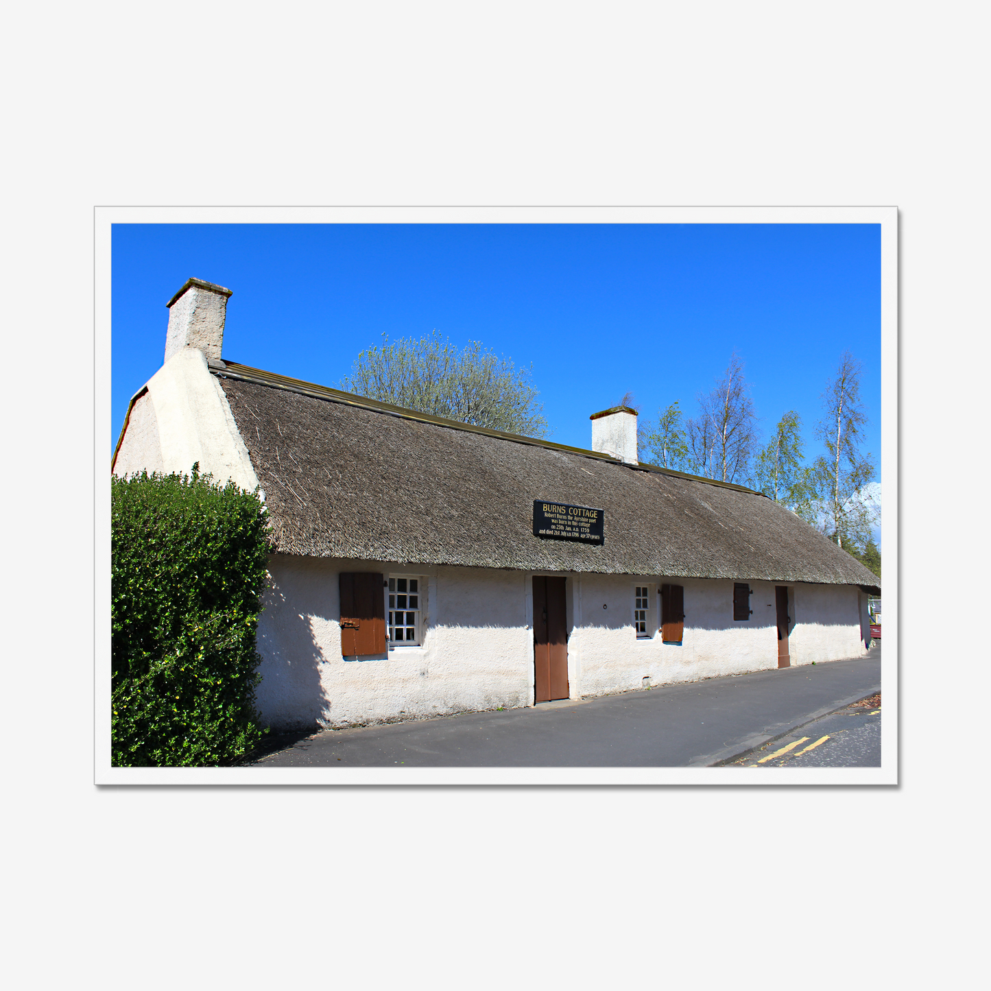 Framed picture of a thatched cottage with a clear blue sky.