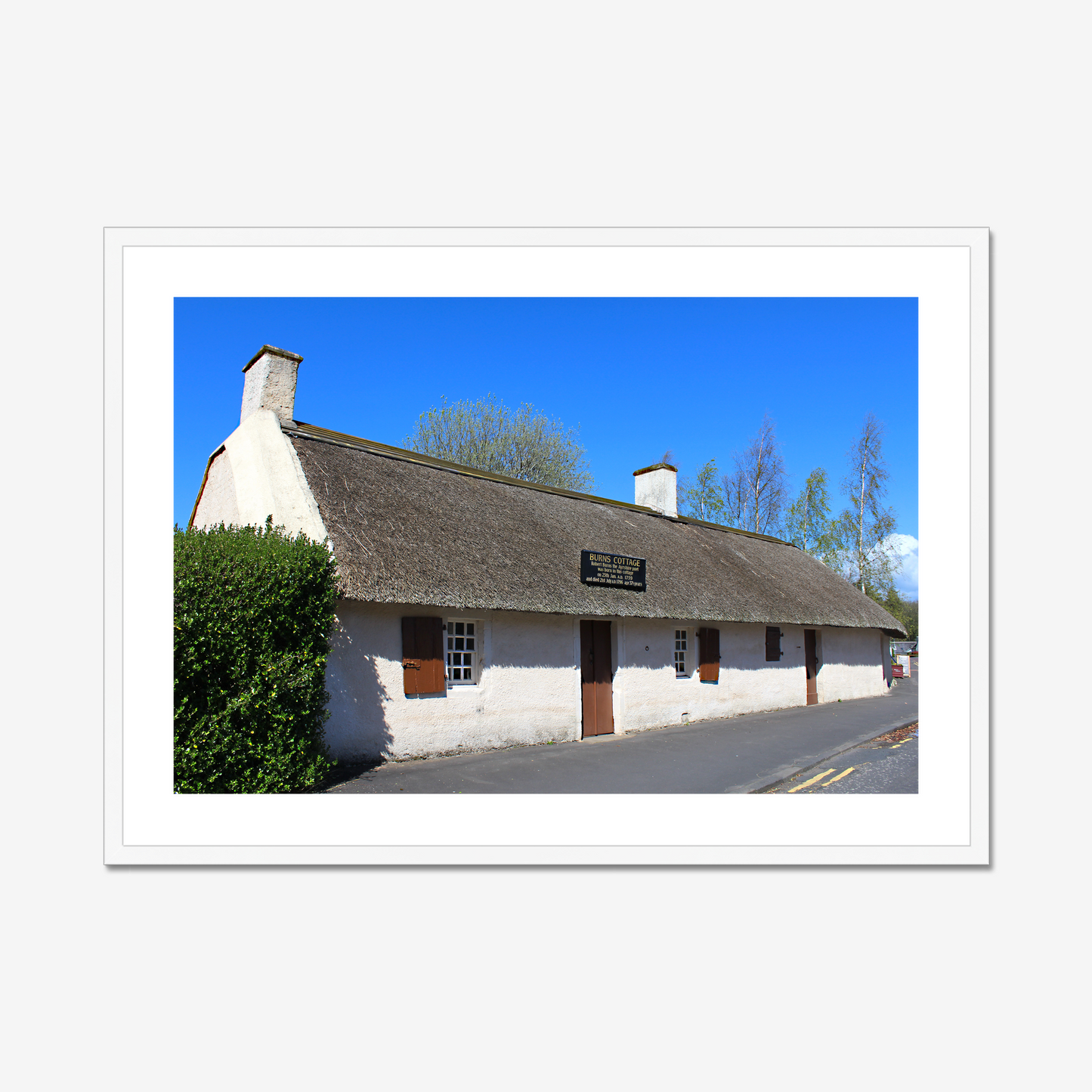 Framed picture of a thatched cottage with a clear blue sky.