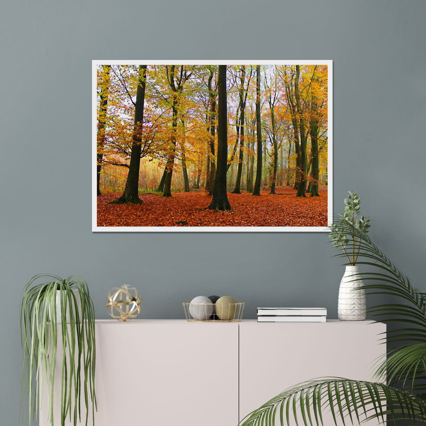 Framed print of a forest scene with autumn colors on a gray wall above a white cabinet.