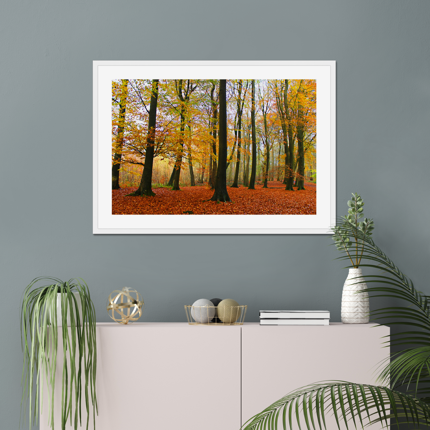 Framed print of a forest scene with autumn colors on a gray wall above a white cabinet.