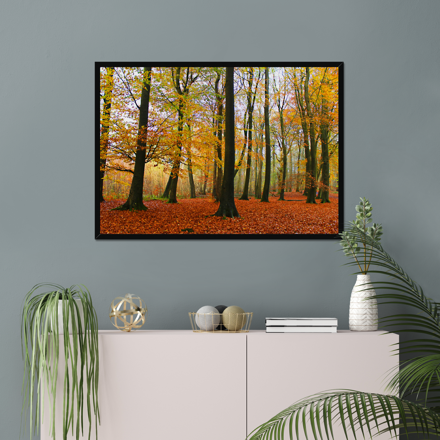 Framed print of a forest scene with autumn colors on a gray wall above a white cabinet.