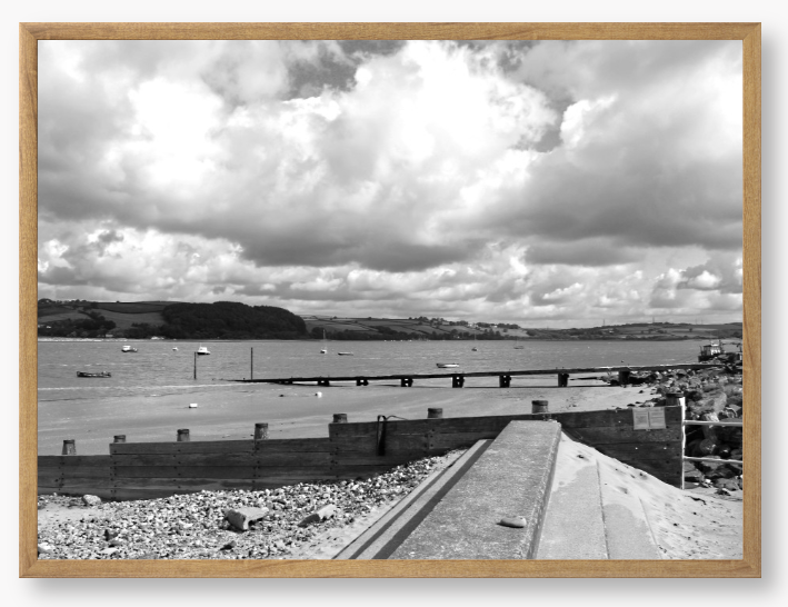 Black and White Framed Photo of a Beach scene with a large body of water, sky with clouds, and distant hills.