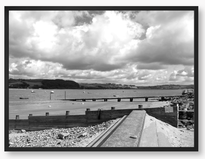 Black and White Framed Photo of a Beach scene with a large body of water, sky with clouds, and distant hills.