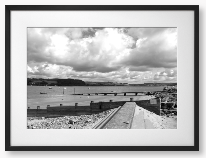 Black and White Framed Photo of a Beach scene with a large body of water, sky with clouds, and distant hills.
