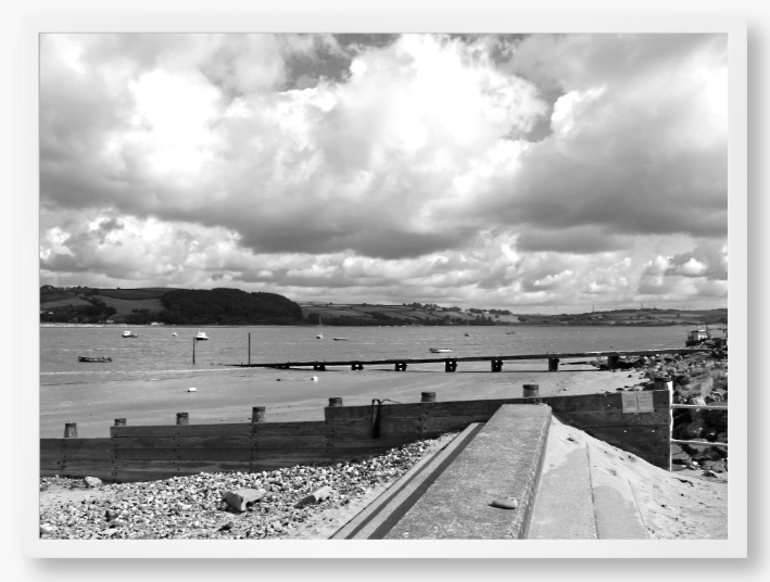 Black and White Framed Photo of a Beach scene with a large body of water, sky with clouds, and distant hills.