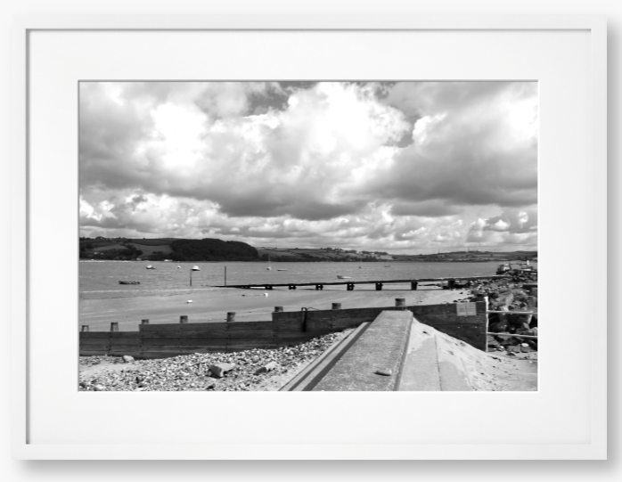 Black and White Framed Photo of a Beach scene with a large body of water, sky with clouds, and distant hills.
