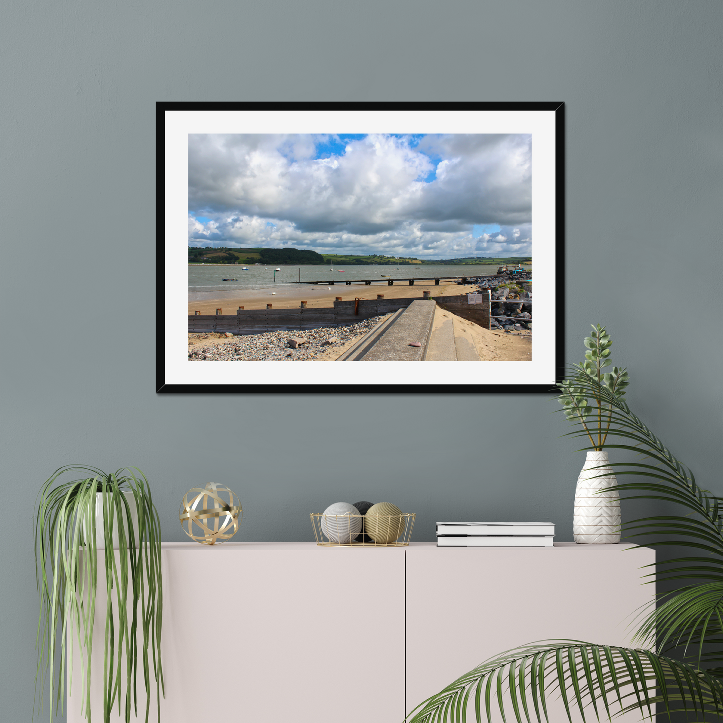 Framed photograph of a coastal scene on a gray wall above a white cabinet with decorative items.
