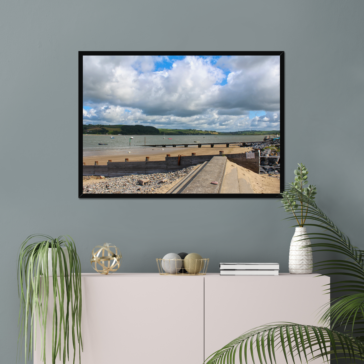 Framed photograph of a coastal scene on a gray wall above a white cabinet with decorative items.