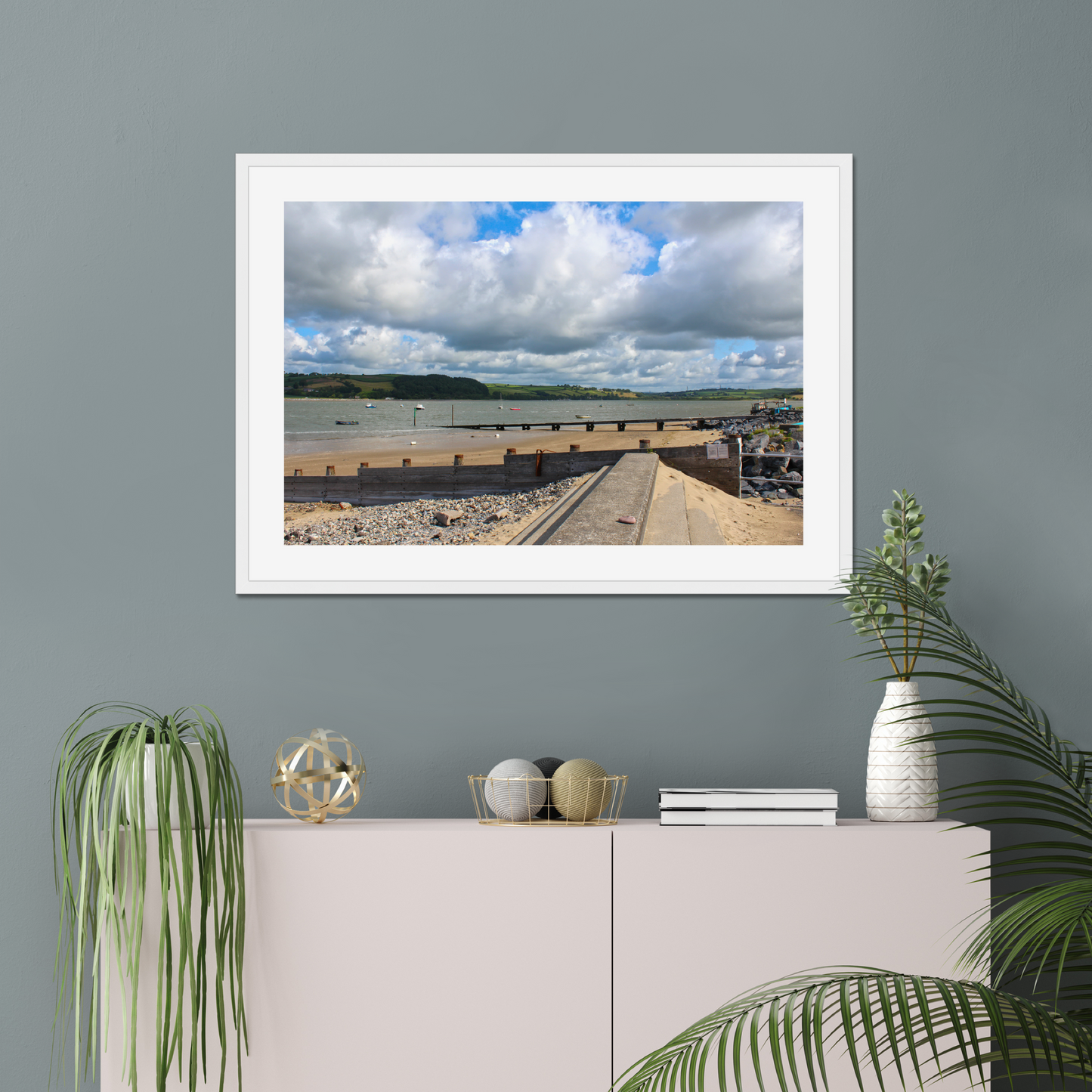 Framed photograph of a coastal scene on a gray wall above a white cabinet with decorative items.