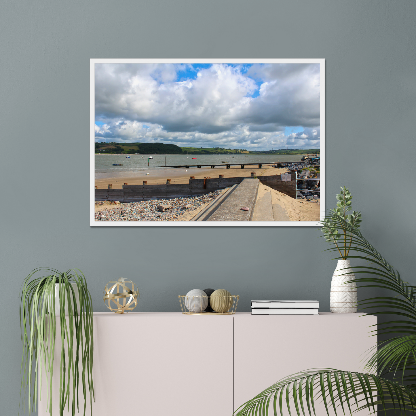 Framed photograph of a coastal scene on a gray wall above a white cabinet with decorative items.