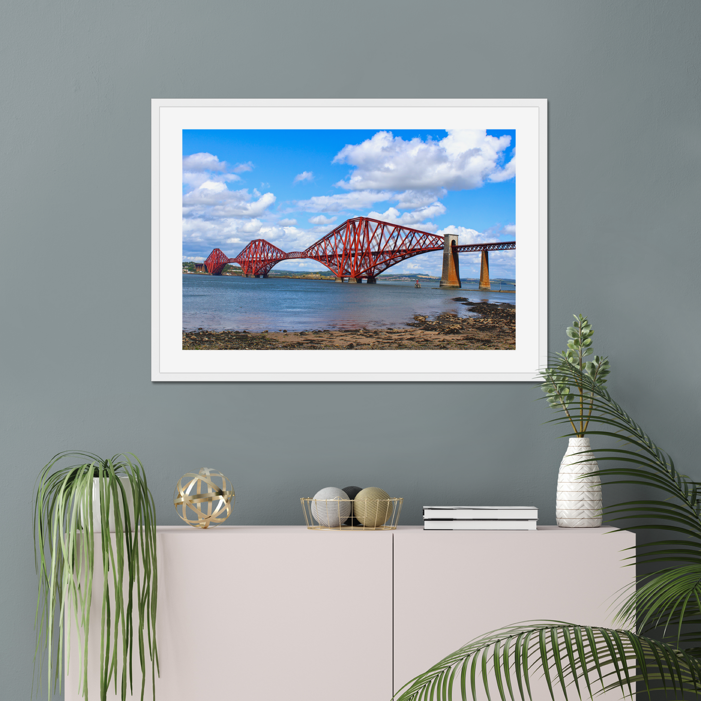 Framed picture of a red bridge over water on a gray wall with decorative items below.