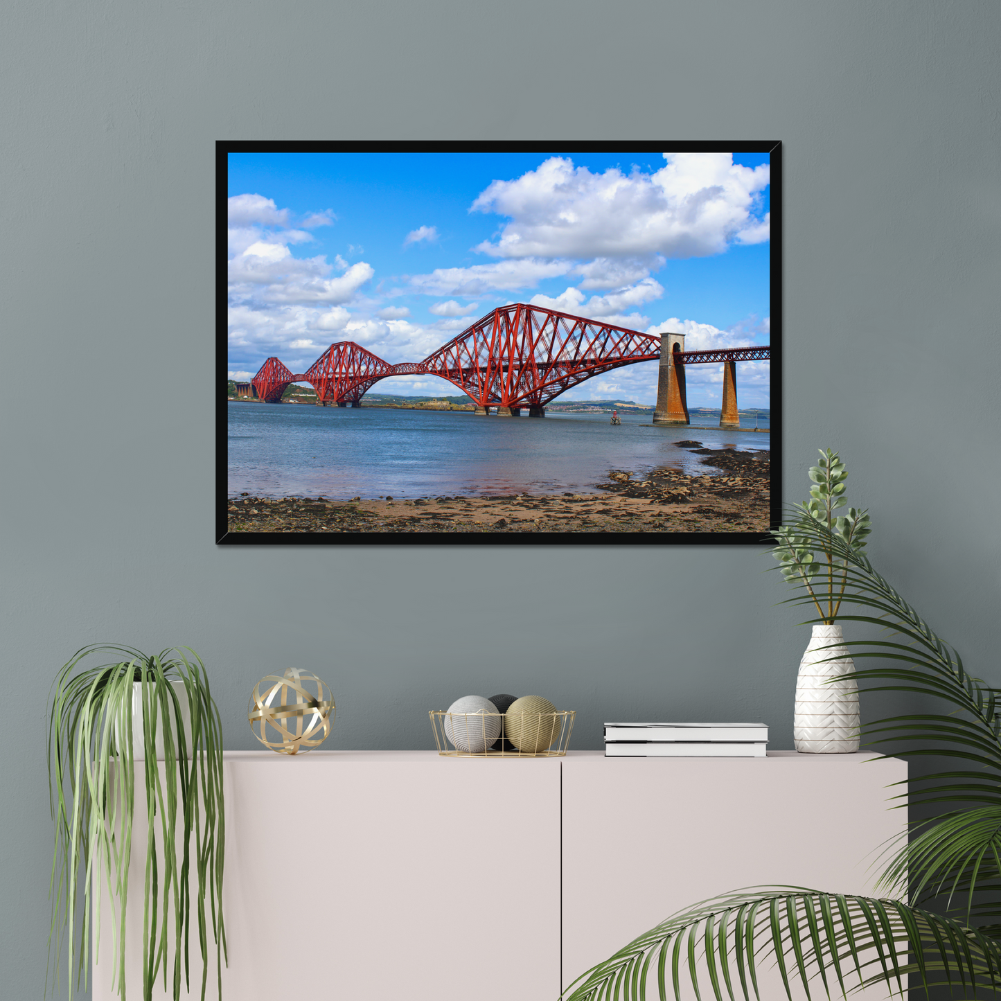Framed picture of a red bridge over water on a gray wall with decorative items below.