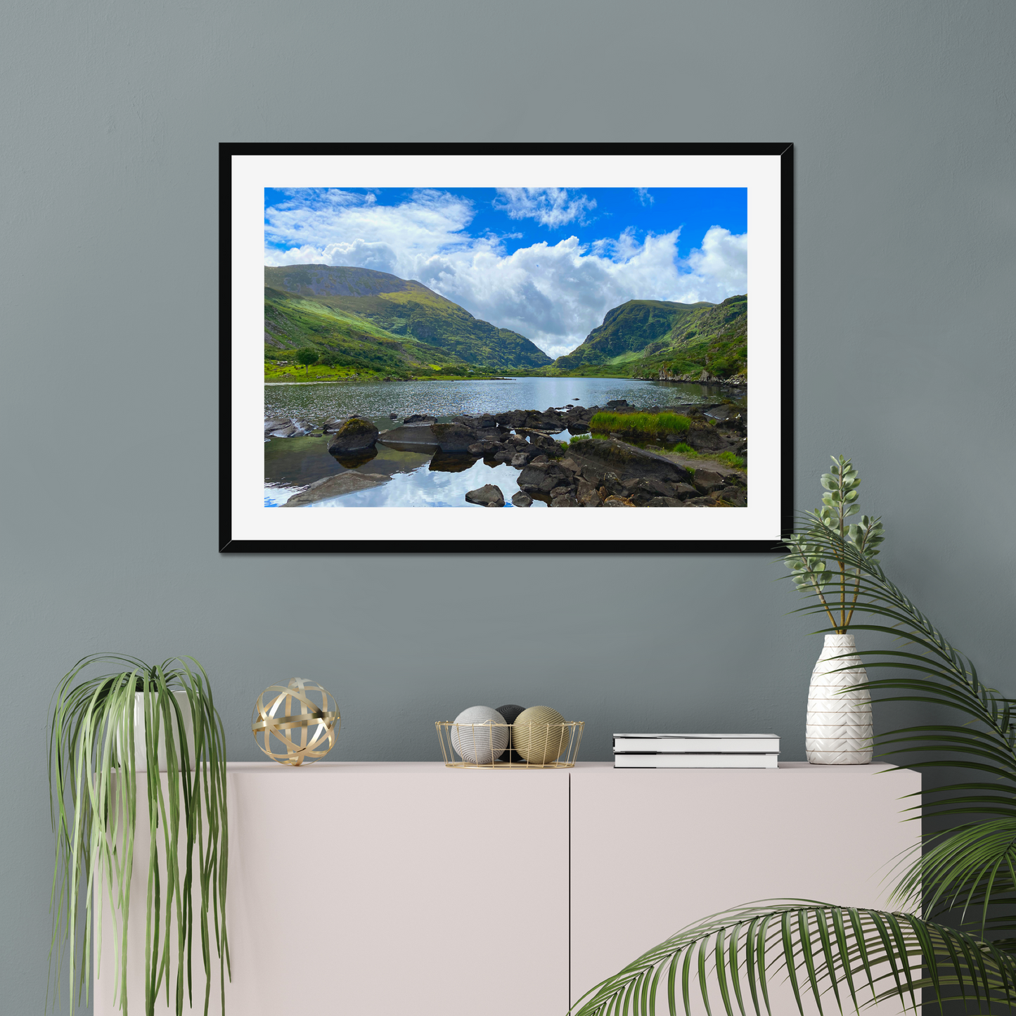 Framed photograph of a lake with mountains in the background on a gray wall with decorative items