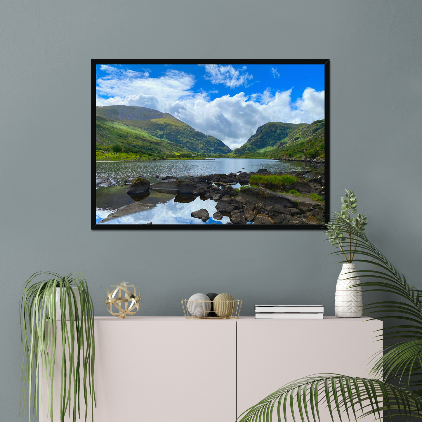 Framed photograph of a lake with mountains in the background on a gray wall with decorative items