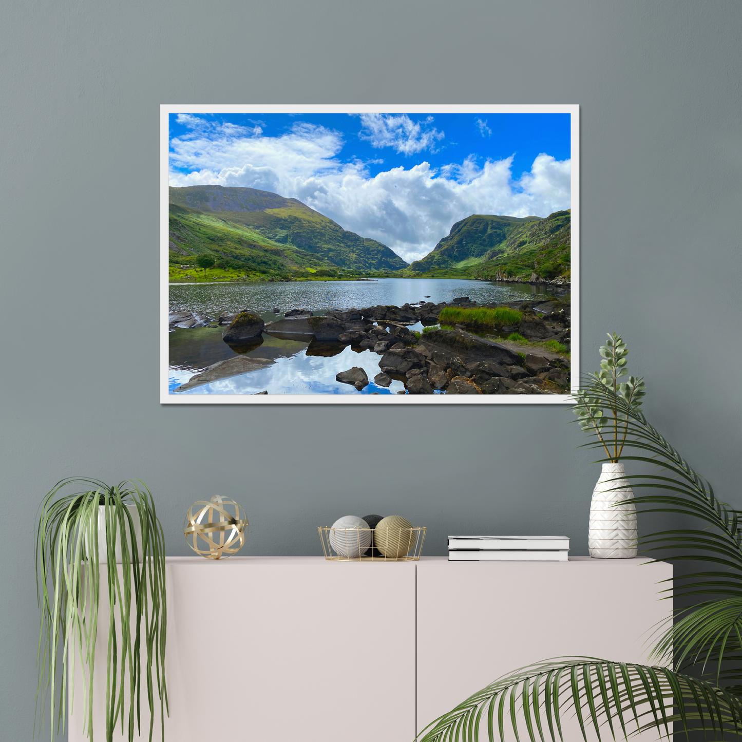 Framed photograph of a lake with mountains in the background on a gray wall with decorative items