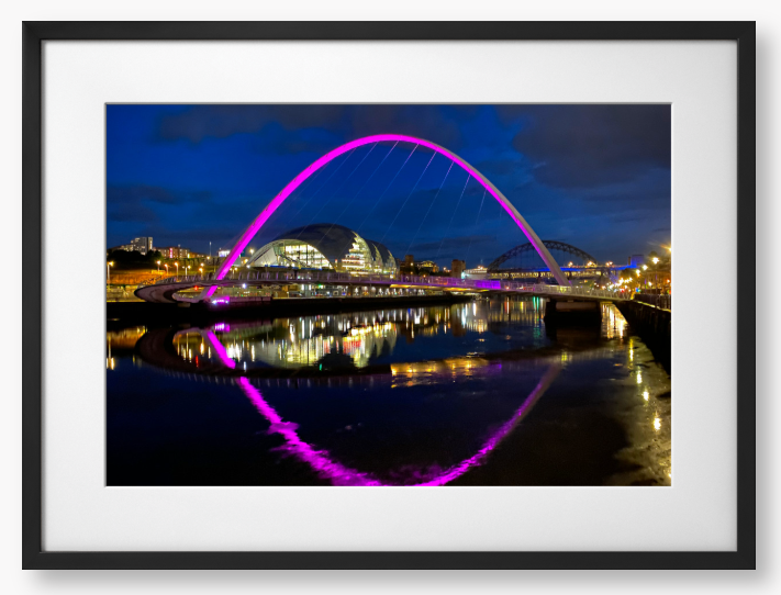 Framed photo of a modern bridge with a purple arch over water at night.