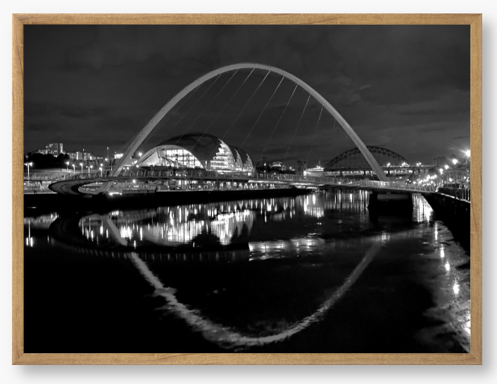 Black and white photograph of a modern bridge over a river at night.