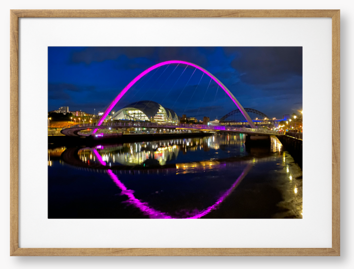 Framed photo of a modern bridge with a purple arch over water at night.