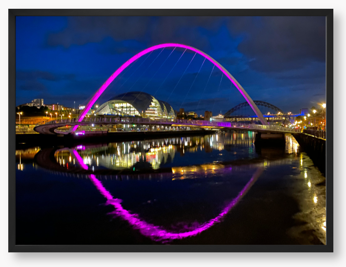 Framed photo of a modern bridge with a purple arch over water at night.