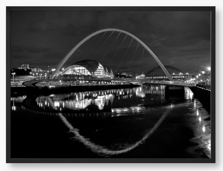 Black and white photograph of a modern bridge over a river at night.