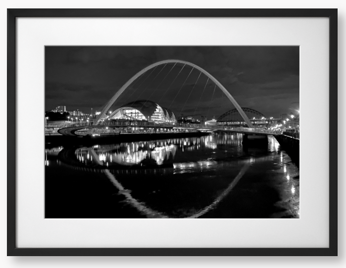 Black and white photograph of a modern bridge over a river at night.