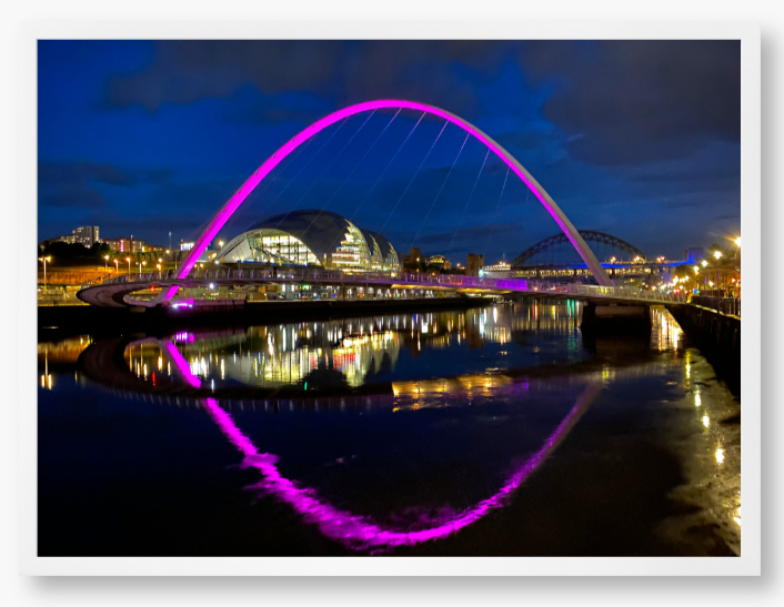 Framed photo of a modern bridge with a purple arch over water at night.