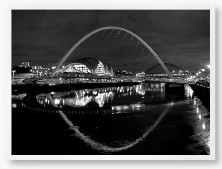 Black and white photograph of a modern bridge over a river at night.