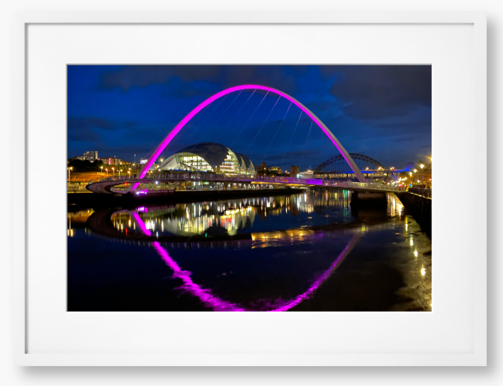 Framed photo of a modern bridge with a purple arch over water at night.