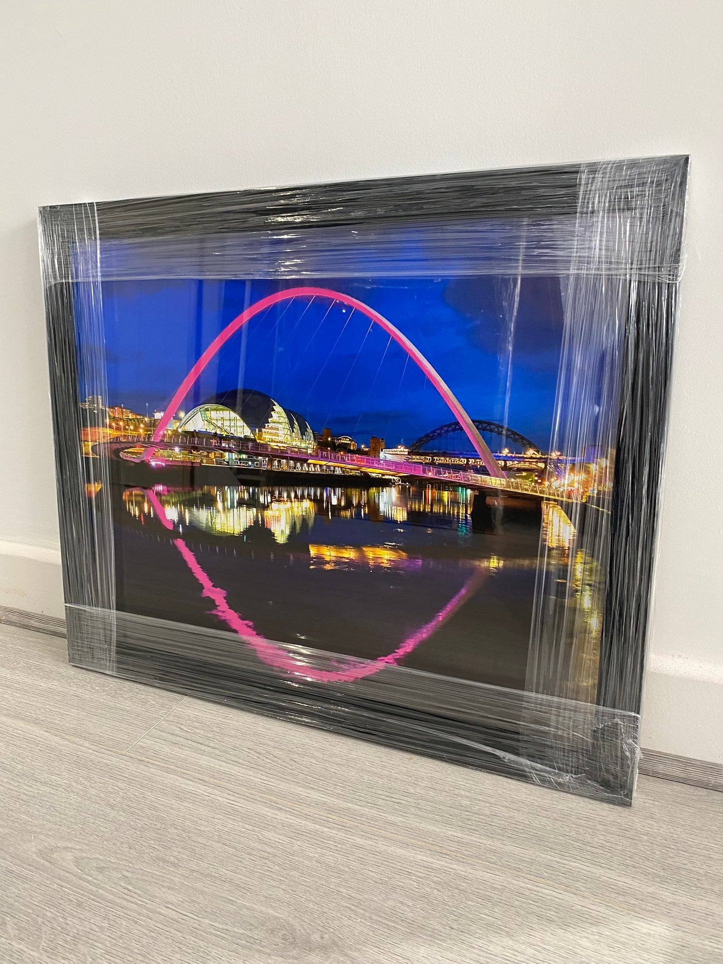 Framed photograph of a colourful arch bridge at night with a reflective water surface.