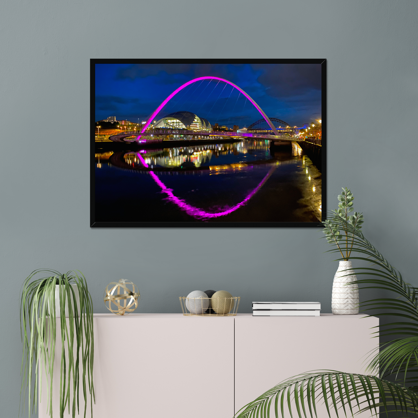 Framed photograph of a bridge with colourful lighting on a wall above a white cabinet with decorative items.