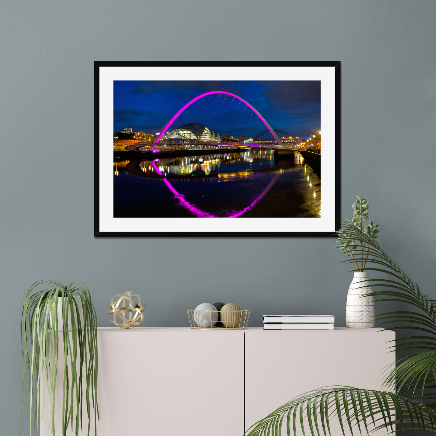 Framed photograph of a bridge with colourful lighting on a wall above a white cabinet with decorative items.