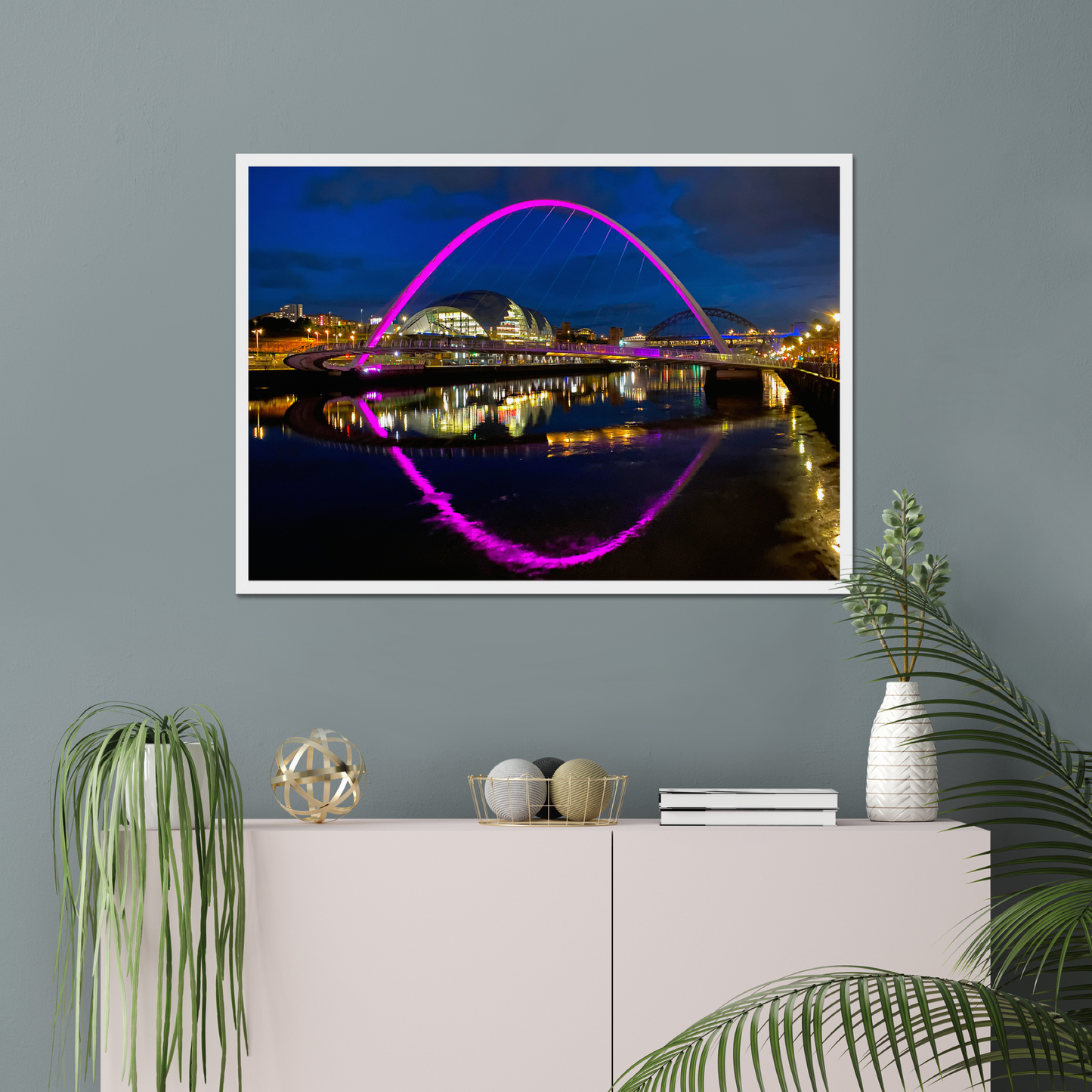 Framed photograph of a bridge with colourful lighting on a wall above a white cabinet with decorative items.