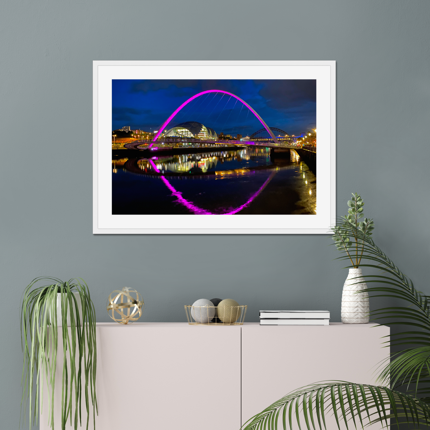 Framed photograph of a bridge with colourful lighting on a wall above a white cabinet with decorative items.