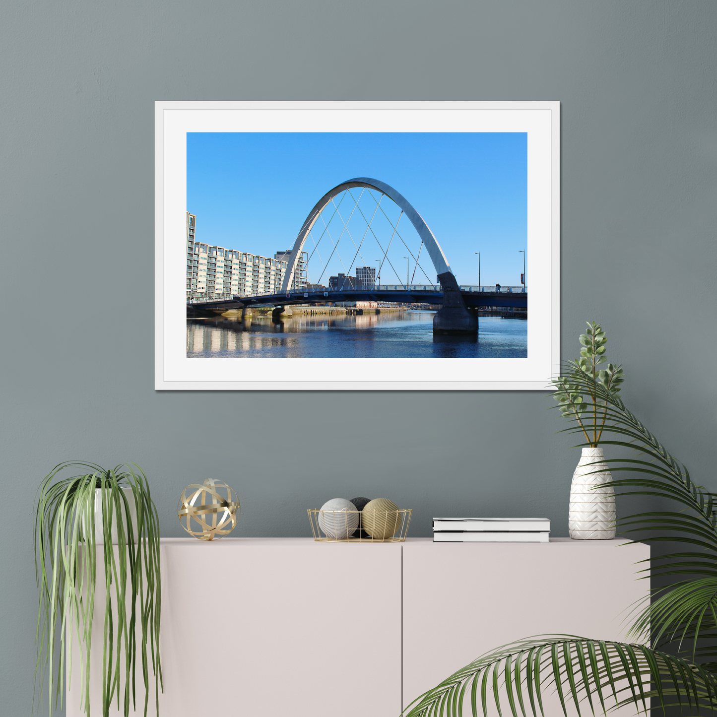 Framed photograph of a cityscape with a bridge on a wall above a white cabinet with decorative items.
