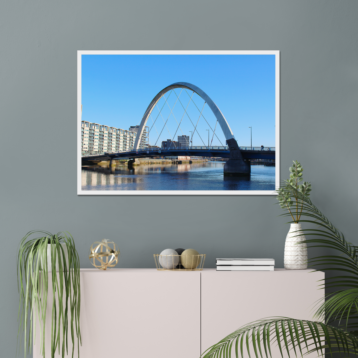 Framed photograph of a cityscape with a bridge on a wall above a white cabinet with decorative items.