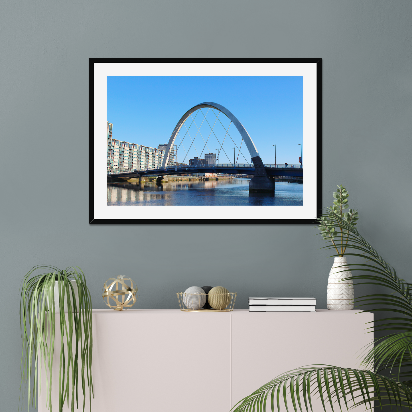 Framed photograph of a cityscape with a bridge on a wall above a white cabinet with decorative items.