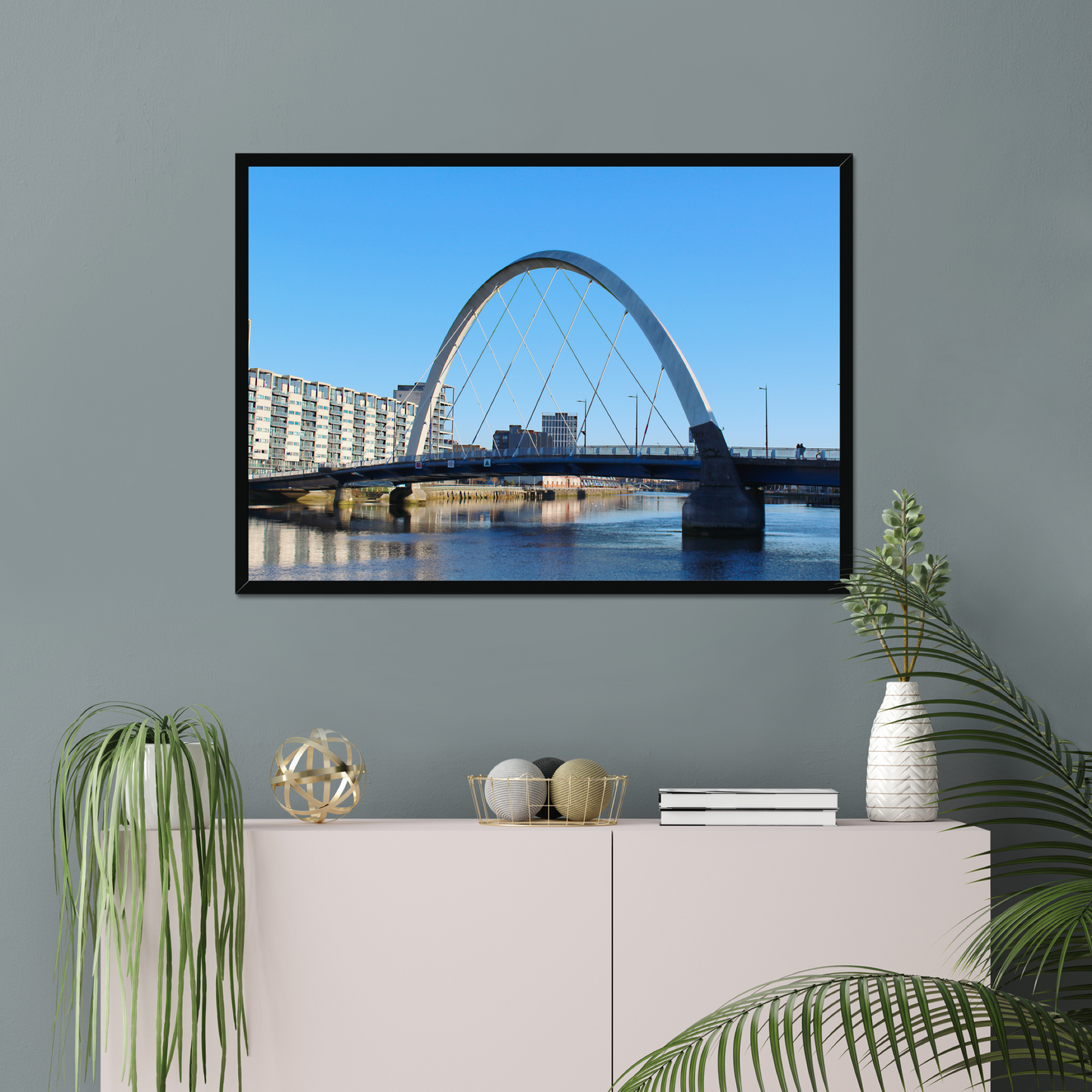 Framed photograph of a cityscape with a bridge on a wall above a white cabinet with decorative items.