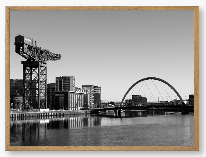 Black and White Framed Photo Of A Cityscape with a crane, buildings, and a bridge over water.