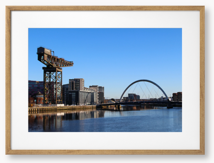 Framed Photo Of A Cityscape with a crane, buildings, and a bridge over water.